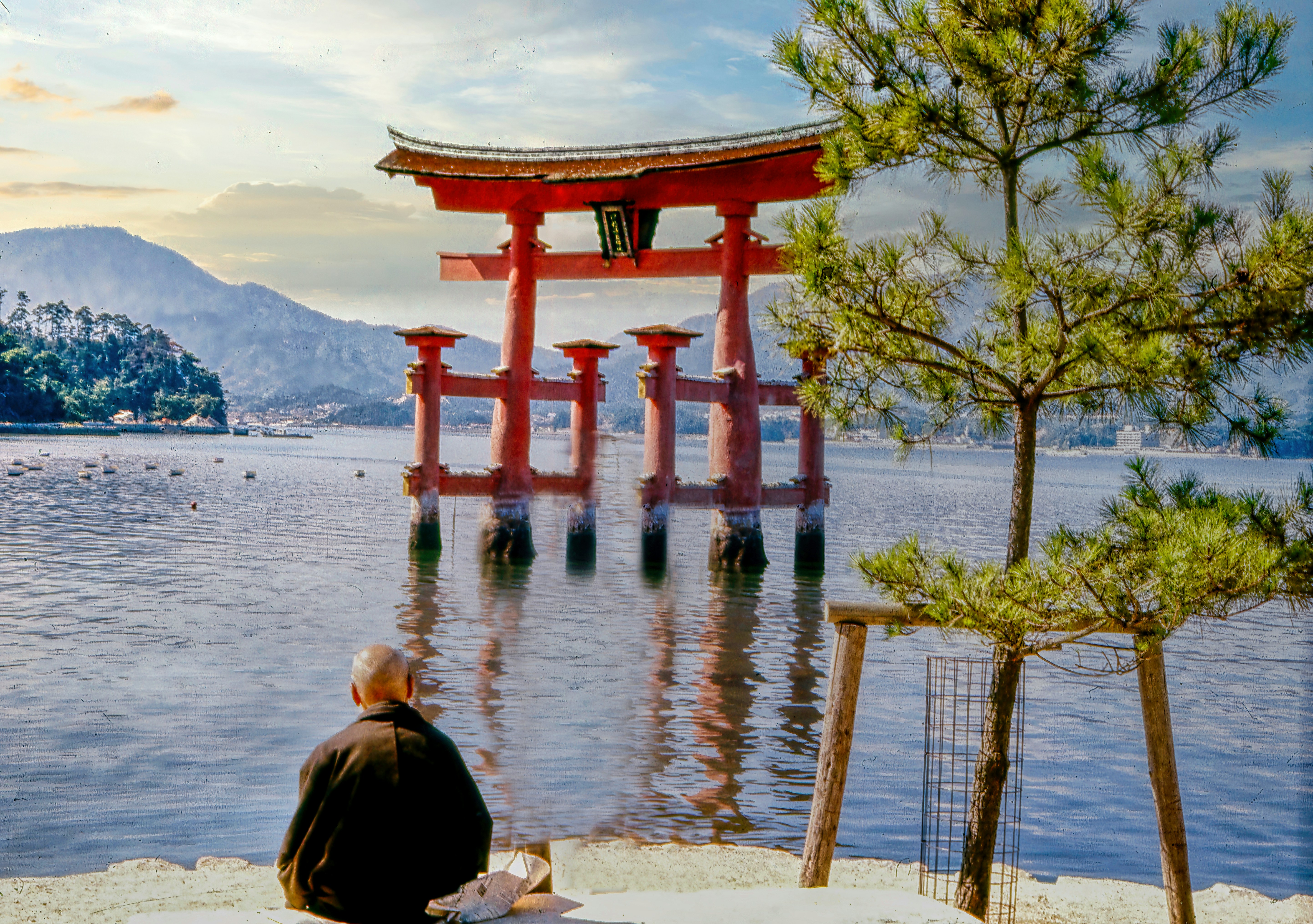 a person sitting on a bench looking at a large red structure in the water, 