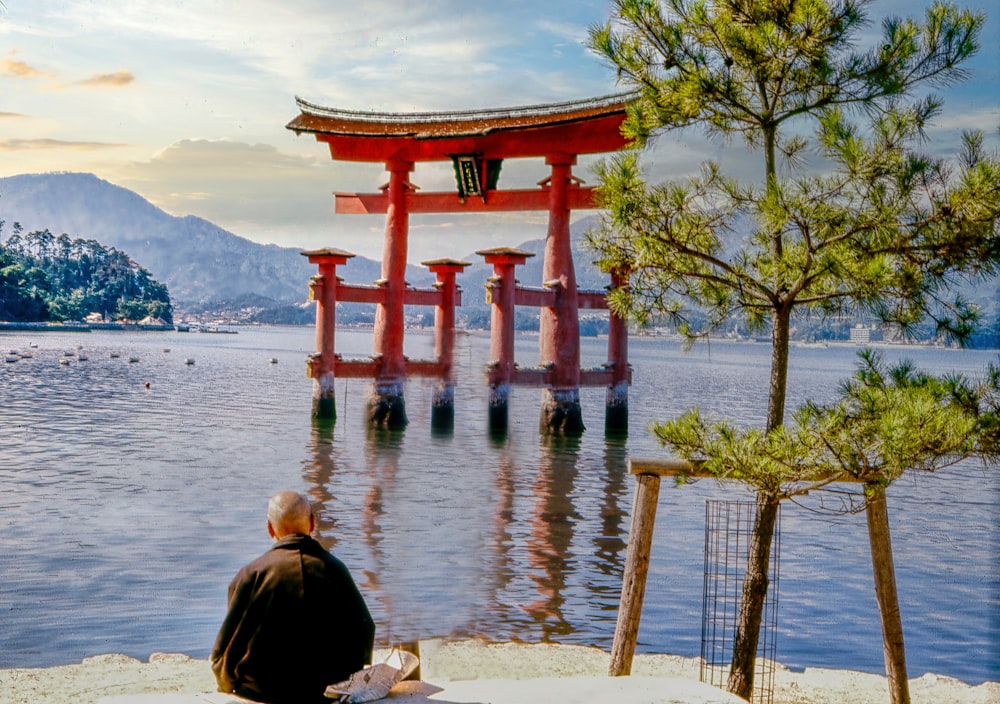 a person sitting on a bench looking at a large red structure in the water