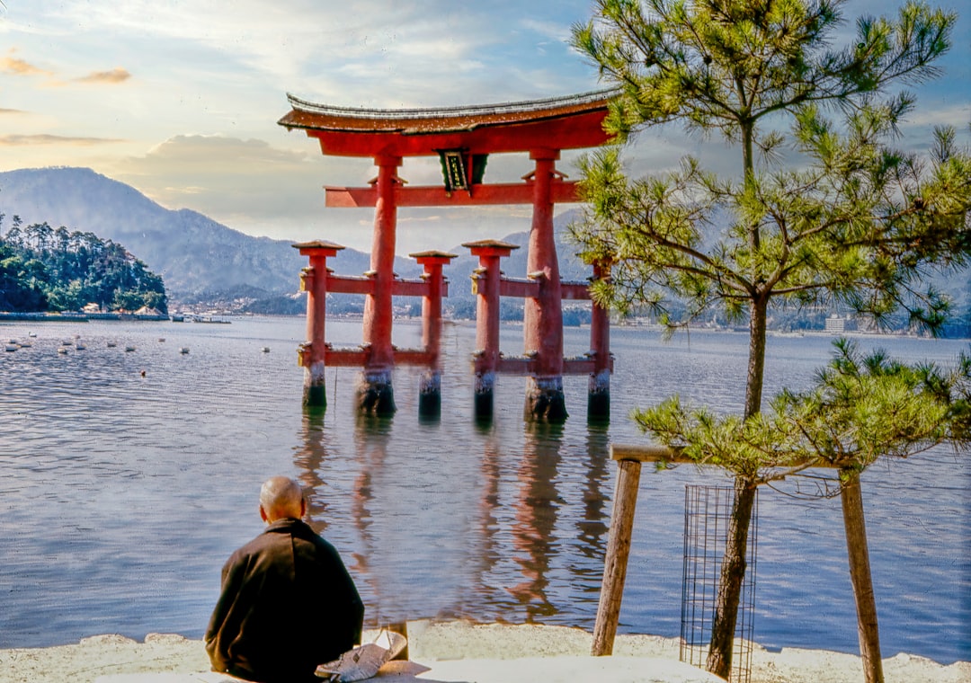 a person sitting on a bench looking at a large red structure in the water,
