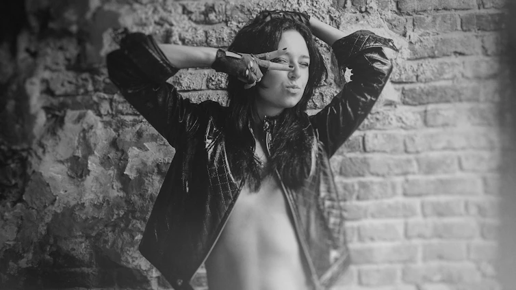 A moody, high-contrast photo of a model wearing oversized black streetwear against a dark urban backdrop with silver accents.