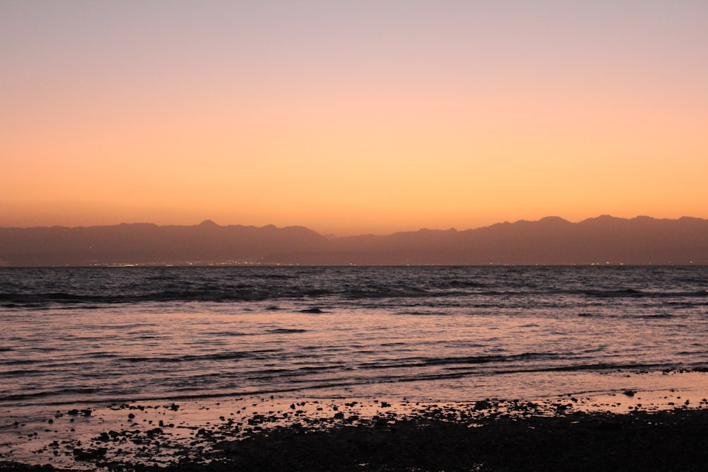 a beach with a body of water and mountains in the background