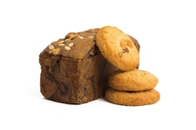 A loaf of bread with a rough texture and seeds on top is positioned next to three stacked round cookies. The bread appears brown, while the cookies are a lighter golden color. The objects are neatly arranged on a white background.