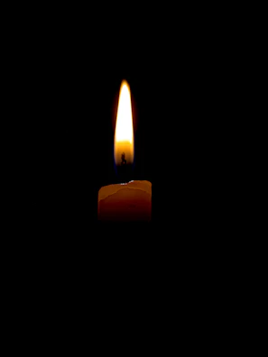 Close-up of a warm yellow candle flickering gently in a dark room.