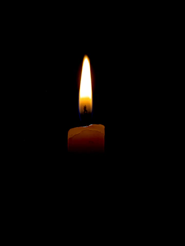 A softly lit candle flame flickering against a desert gold background, symbolizing hope and remembrance.