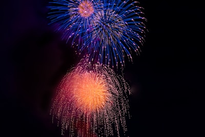 Brightly colored fireworks explode against a dark night sky, featuring vibrant bursts of blue and orange with a dazzling array of lights and trails.