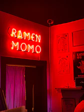 A cozy takeaway counter with warm lighting and the Kraze Momo logo glowing softly on a deep maroon wall.
