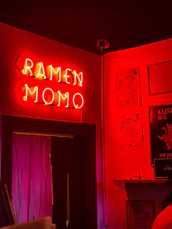 A cozy takeaway counter with warm lighting and the Kraze Momo logo glowing softly on a deep maroon wall.