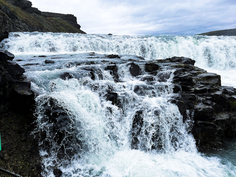 a waterfall with rocks and a cloudy sky