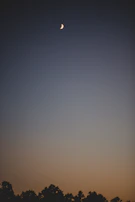 Crescent moon slowly rising on the horizon with soft orange hues.