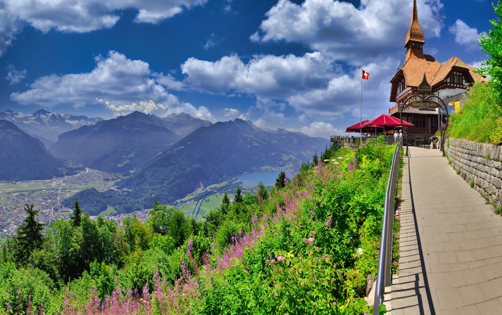 a building with a steeple and a hill with trees and mountains in the background