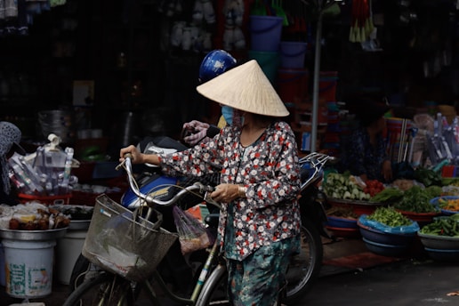 Local woman wearing a Non La conical hat pushing a bicycle with a basket in a Vietnamese market