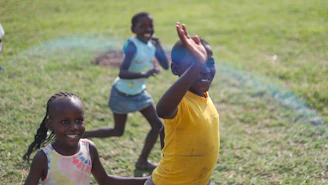 Young children playing football joyfully on a sunny field, symbolizing hope and growth.