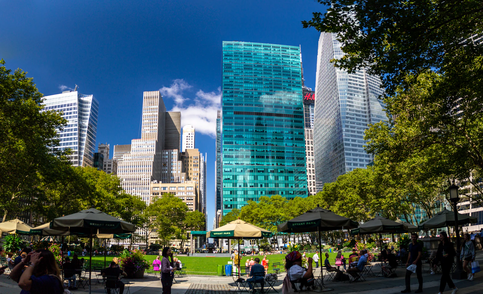 Travel photograph: People sitting and walking in green Bryant Park with Midtown towers rising closely around it.