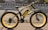 A black and yellow electric bicycle with thick tires is parked on the side of a paved road. The bicycle features branding and text on the frame and wheels, and has a sturdy, modern design. It is located in an urban setting with a road and buildings in the background.