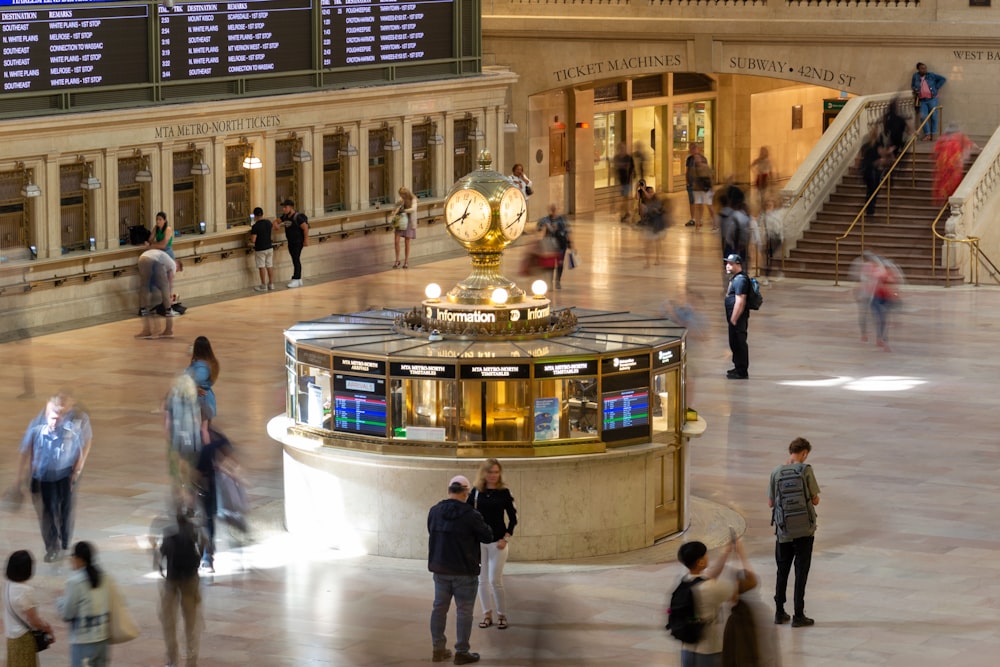 a large room with people and a gold clock on a stand