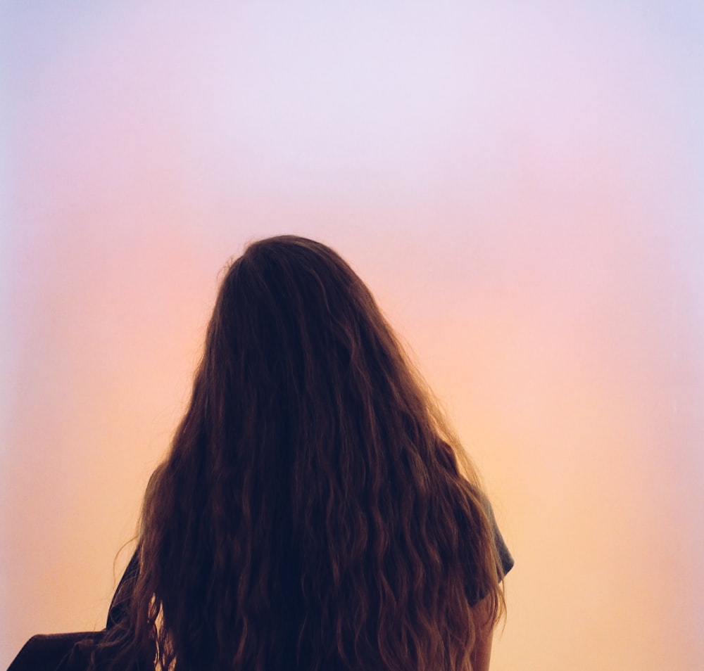 a woman's back with a pink and purple sky in the background