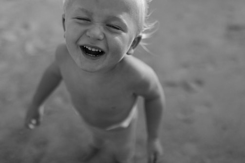 A child with blonde hair is laughing joyfully, looking up, and is captured in a grayscale image. The focus is on the child's expression, conveying happiness and playfulness.