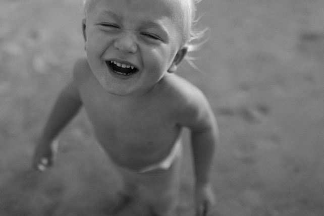 A child with blonde hair is laughing joyfully, looking up, and is captured in a grayscale image. The focus is on the child's expression, conveying happiness and playfulness.