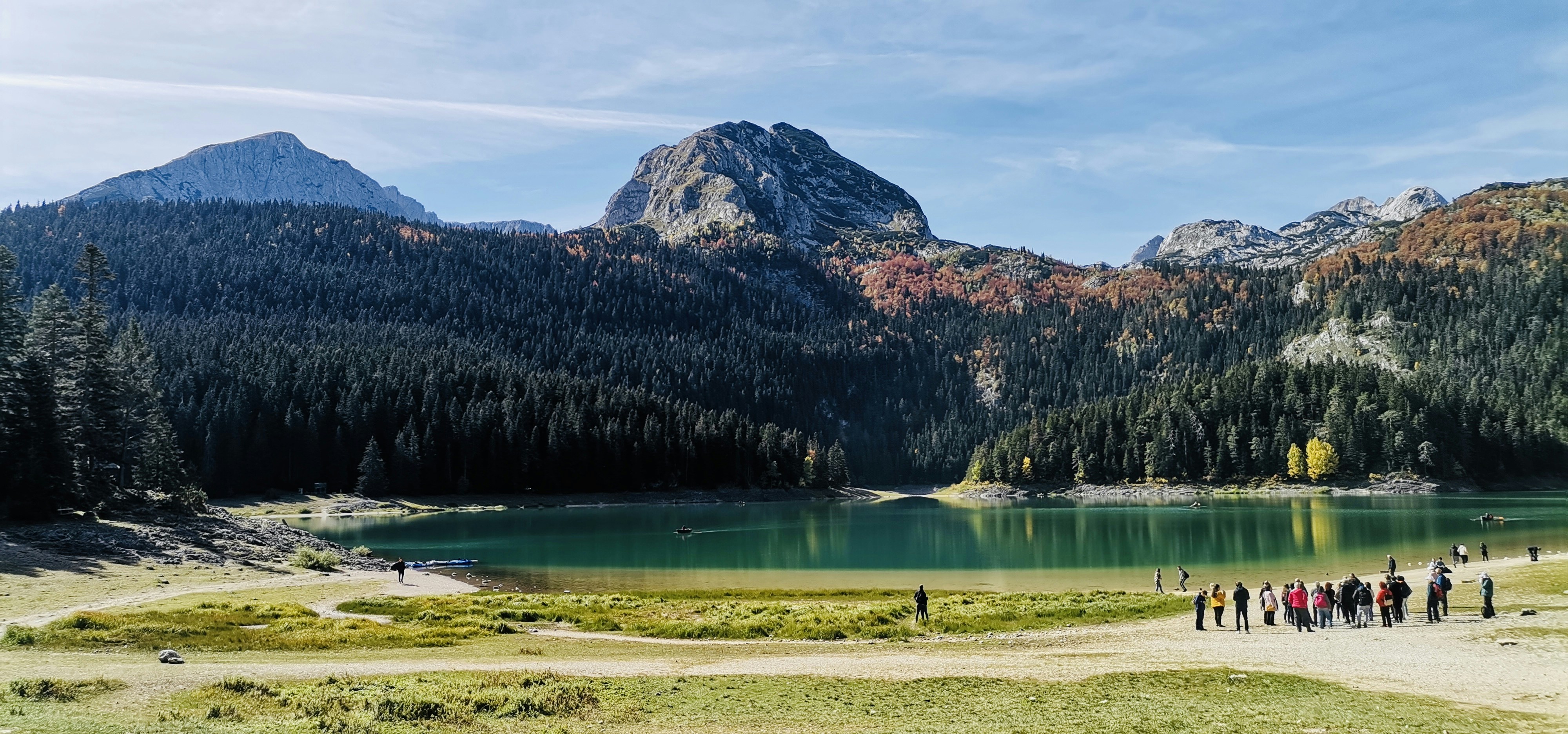a group of people walking along a lake in front of mountains