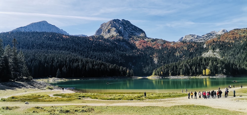 a group of people walking along a lake in front of mountains