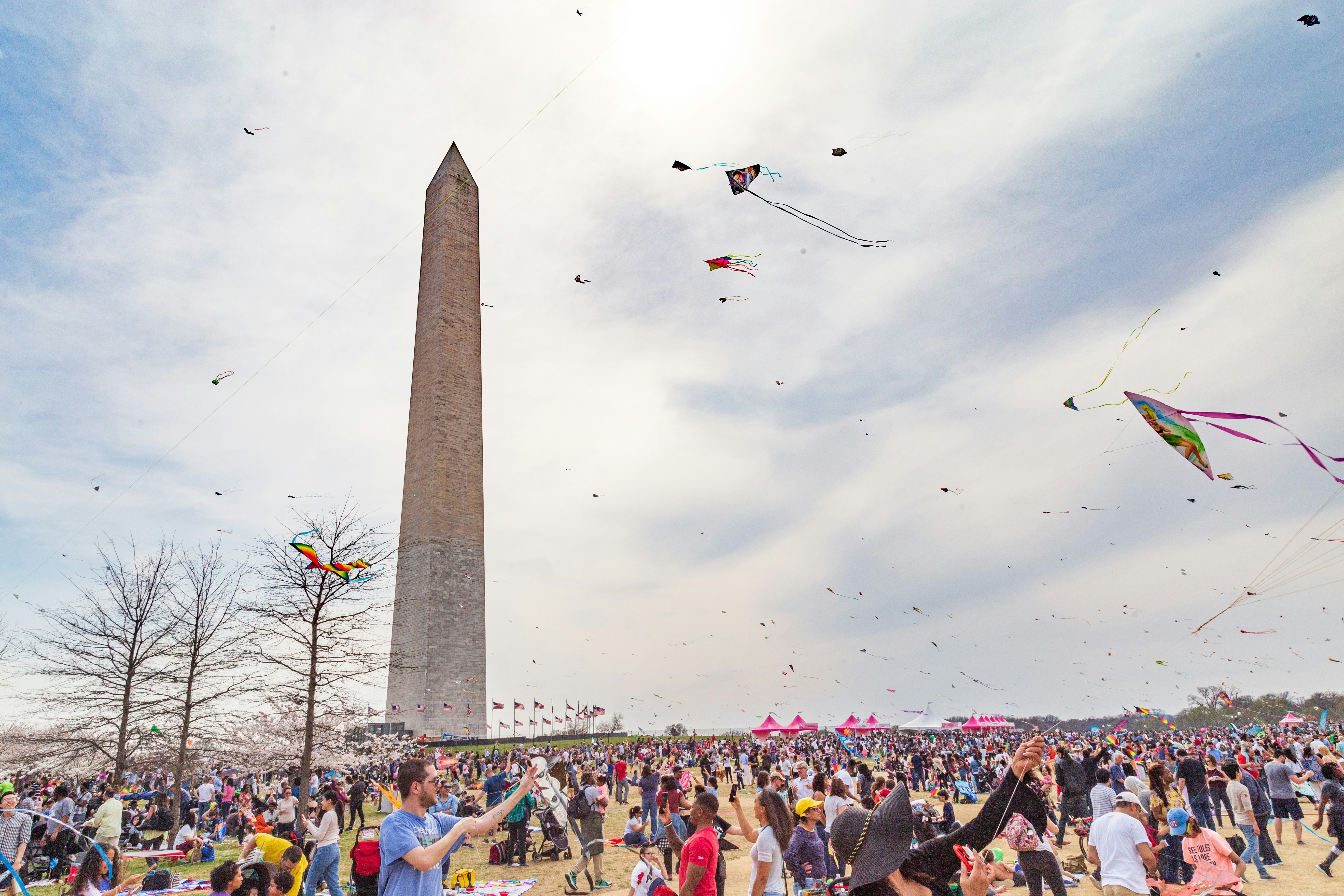 a crowd of people flying kites with Washington Monument in the background