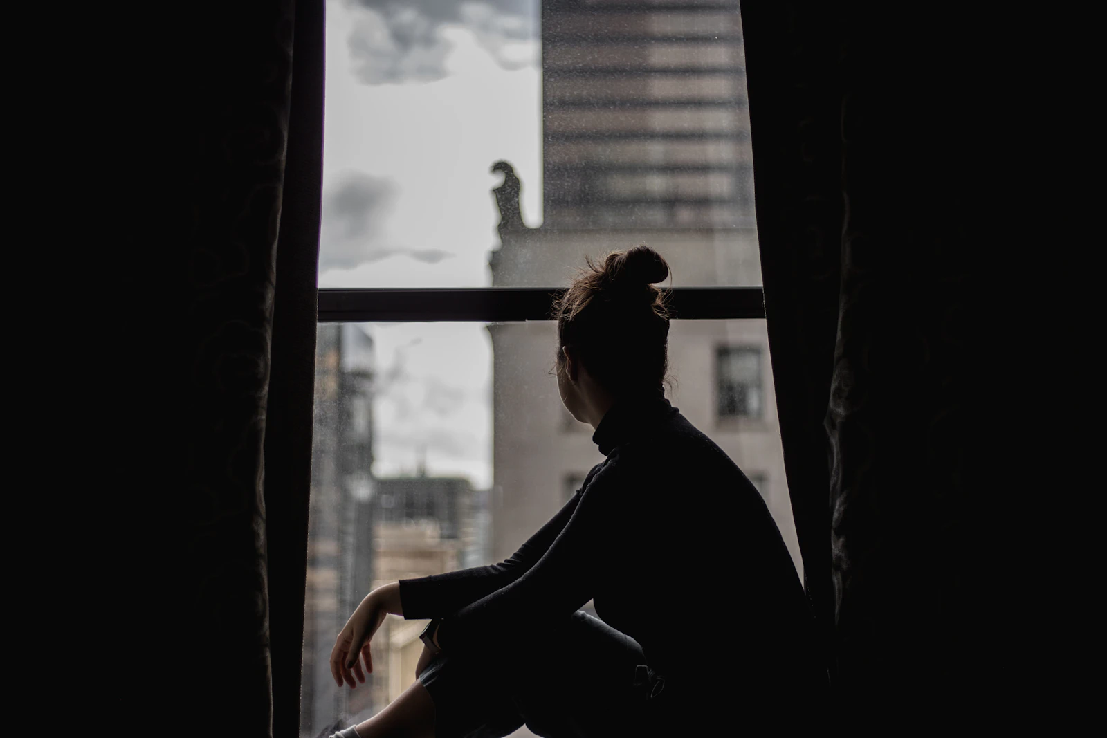 Person sitting alone by a window while feeling conflicted about a relationship