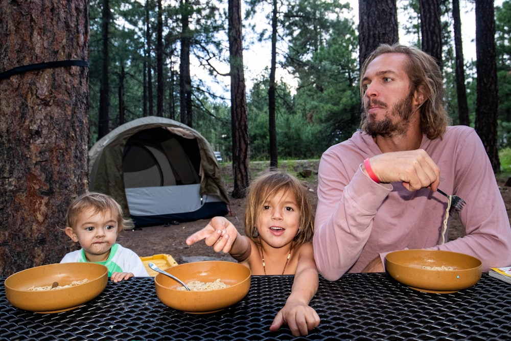 a person and two children sitting at a table with food