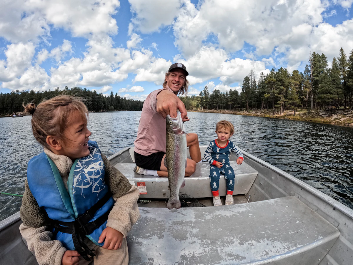 A dad shows off his catch to two young kids in life jackets in a tinnie