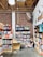 A cozy bookstore with wooden bookshelves filled with colorful books lining the walls. A woman and a child sit on the floor in a corner reading a book, accompanied by a fluffy white dog. The setting has an exposed brick wall and wooden ceiling beams, creating a warm and inviting atmosphere.