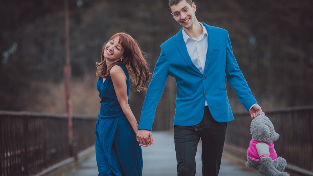 a man and woman holding hands and walking with a teddy bear