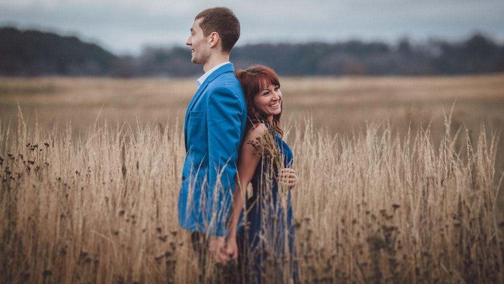 a man and woman standing in a field of tall grass