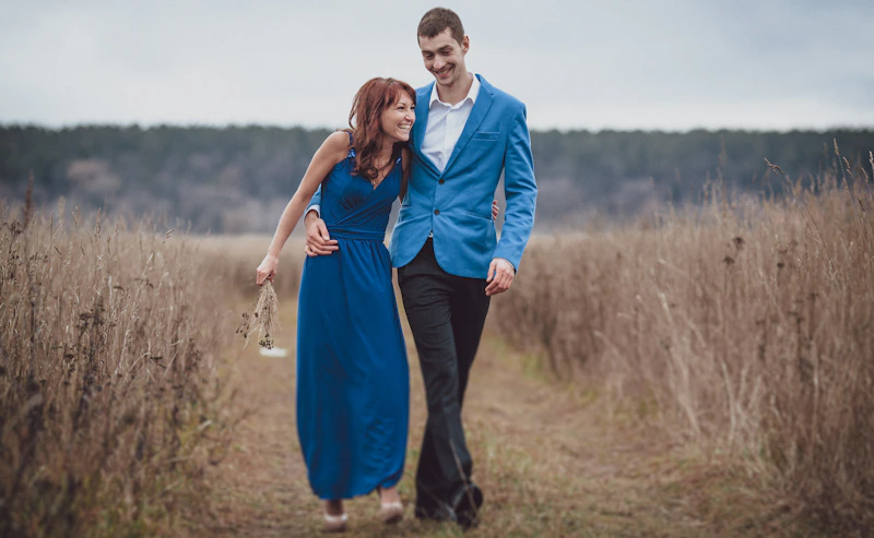 couple holding hands while walking through a field