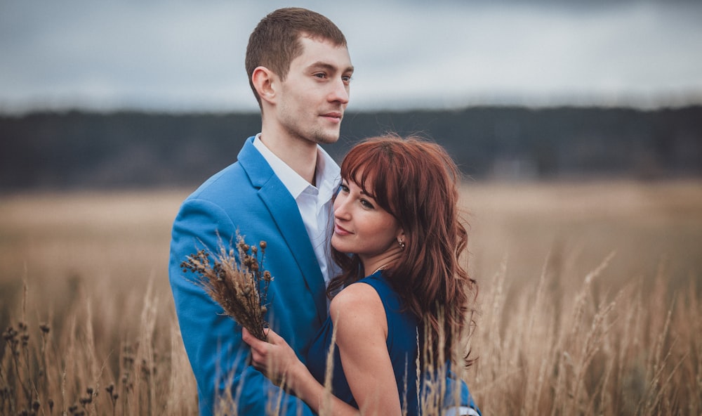 a man and woman standing in a field of tall grass