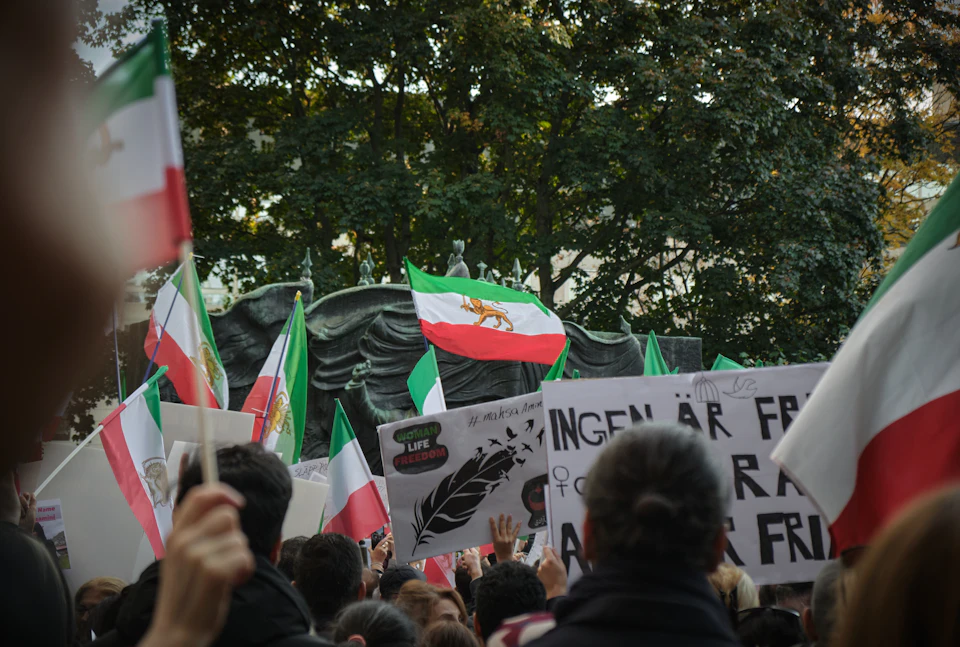 Large crowd gathers on street lined with trees holding signs and flags