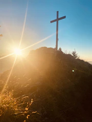 A serene sunrise behind a cross on a hilltop.