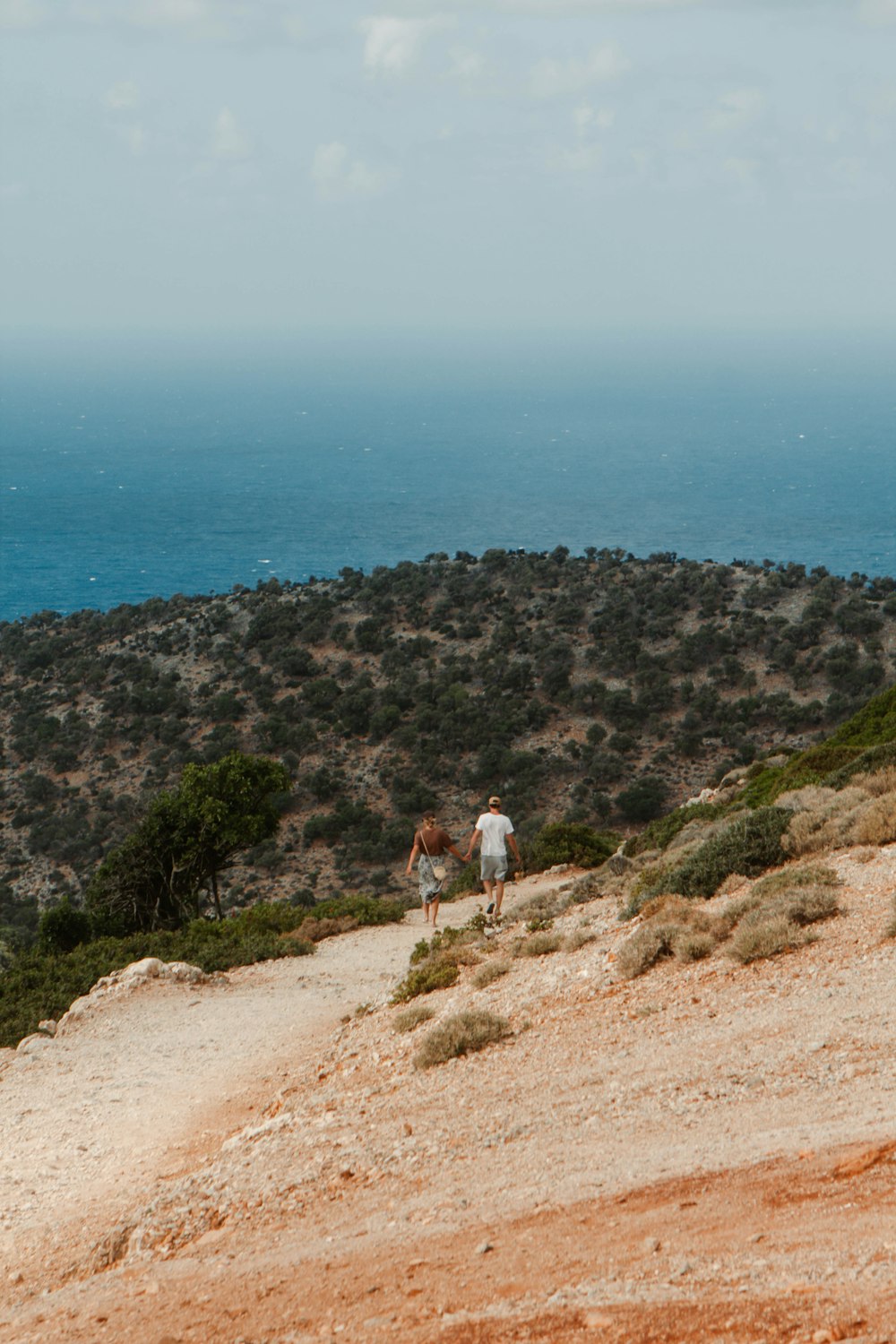 a couple people walking on a dirt path by a body of water