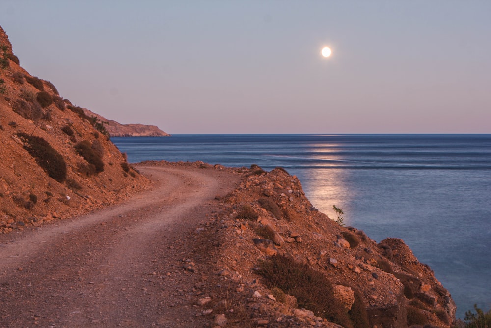 a sandy beach with a body of water and a moon in the sky