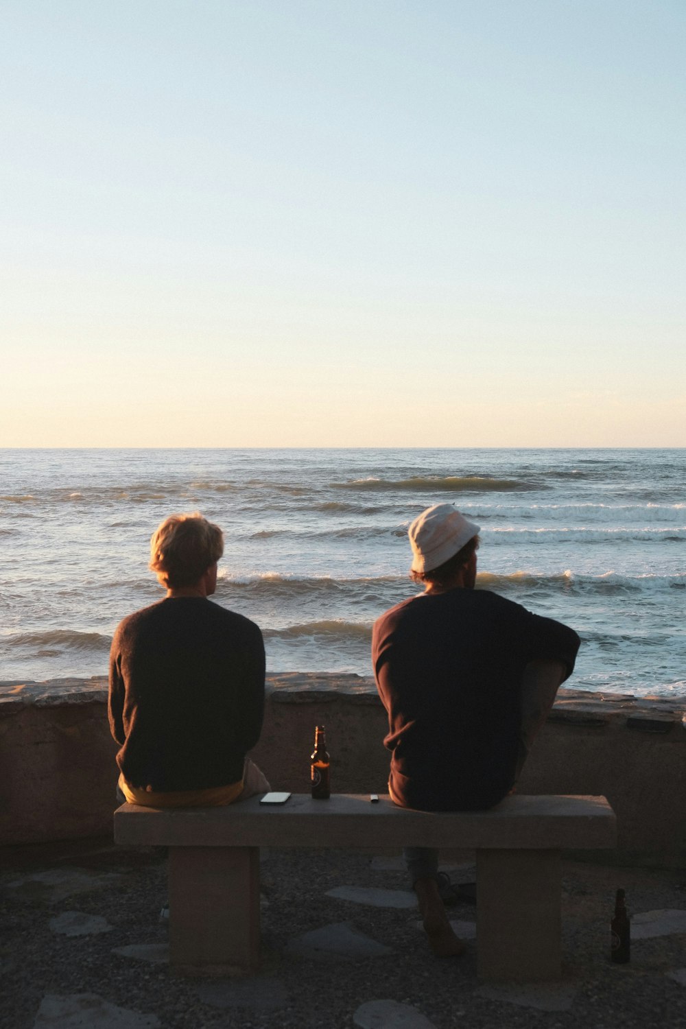 two people sitting on a bench looking at the ocean