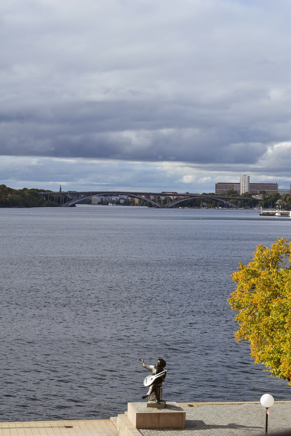 a statue on a platform by a body of water with a bridge in the background