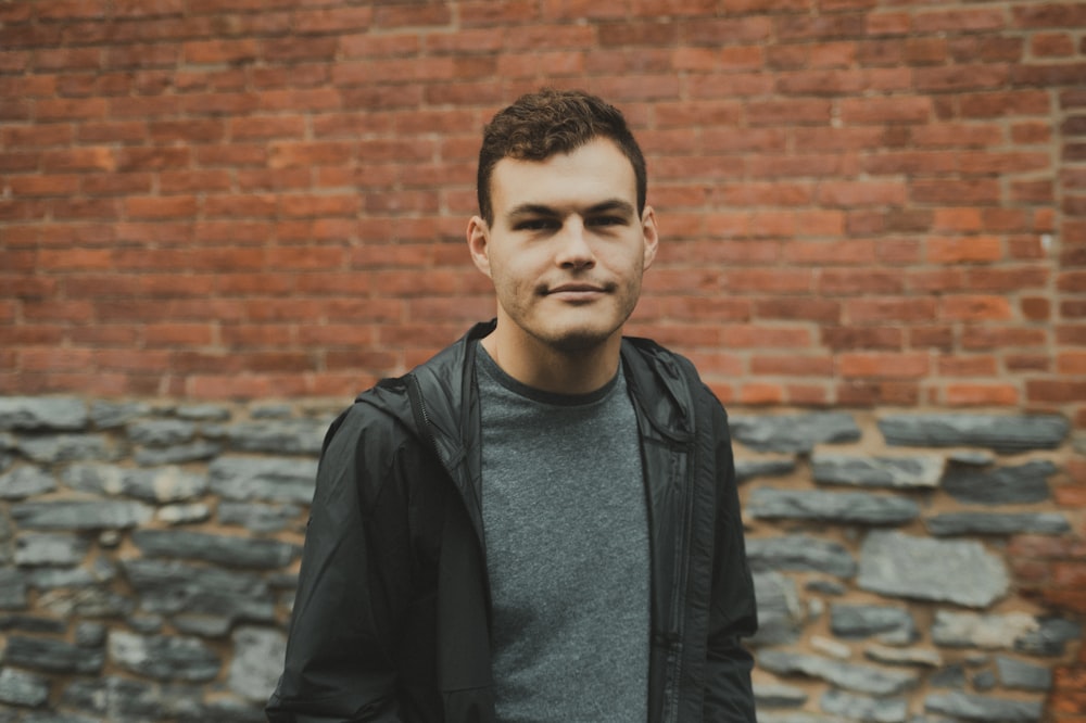 a man standing in front of a brick wall