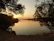A serene lakeside timber estate at sunset with warm light reflecting on calm water and tall pine trees.