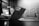 A black and white image showing a laptop with 'HERO GRAPHX' sticker in a modern office setting. The focus is on the laptop, while the background is softly blurred, including a table, chairs, and patterned wall.