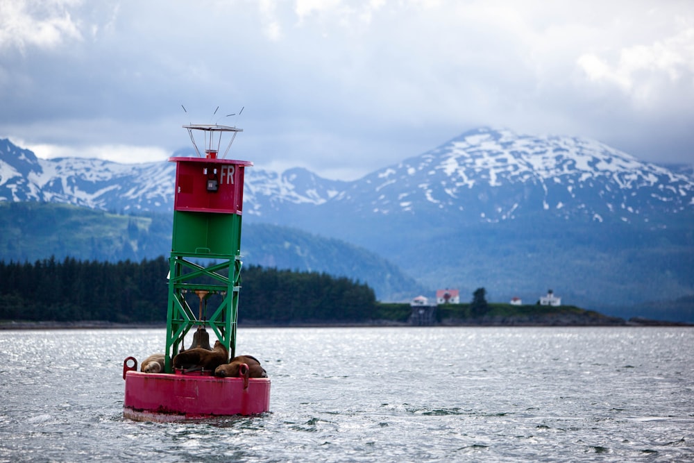 a red and green tower in the middle of a lake with mountains in the background