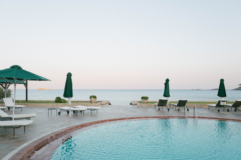 a pool with lounge chairs and umbrellas by a beach