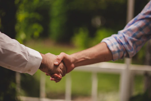 Two people shaking hands in front of a blurred green garden
