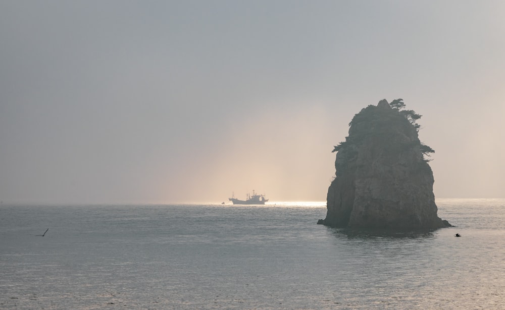 a large rock in the middle of the ocean with a large ship in the distance