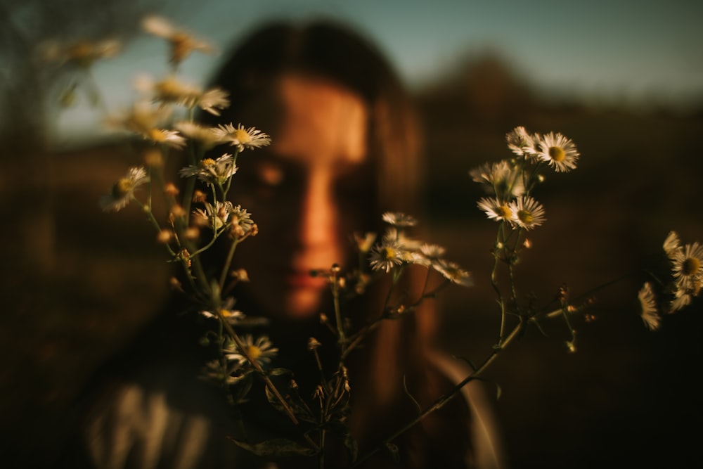 a person's face behind a plant with white flowers