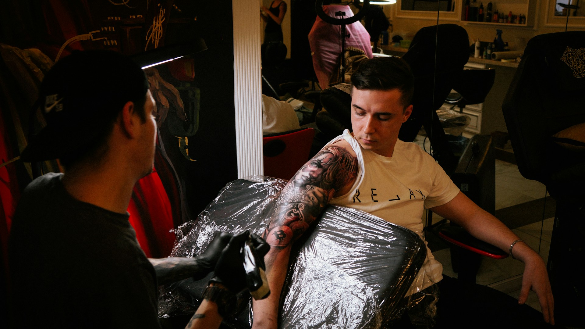 An artist's hand carefully shading a detailed black and grey tattoo on a forearm in a bright, welcoming studio.