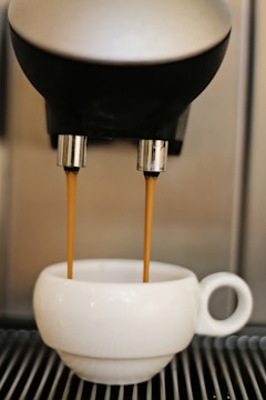a white coffee maker pouring coffee into a white cup
