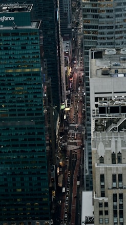 Aerial view of a city street lined with tall buildings, capturing the vibrant energy of urban life. Traffic and lights illuminate the scene, creating a dynamic visual contrast with the towering structures around.